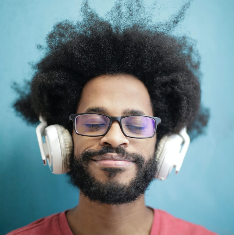A black man with an afro listens to music while his eyes are closed and he smiles.
