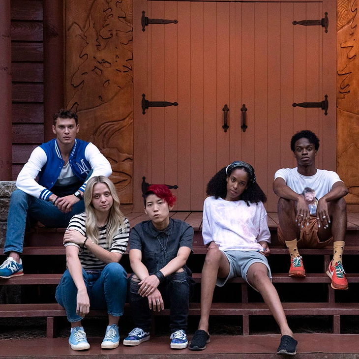 The teens in the camp sitting on the steps at the front door with serious expressions on their faces.