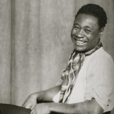 Black and white image of Claude McKay smiling sitting on a chair.