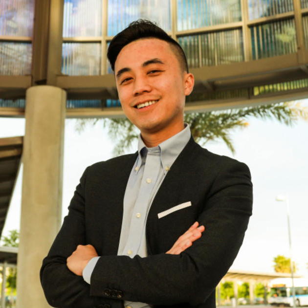 Alex Lee smiling while crossing his arms near an outdoor building.