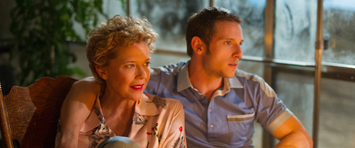 Gloria and Pete sitting side by side at a table. Pete has his arms around her while they look at someone out of frame.