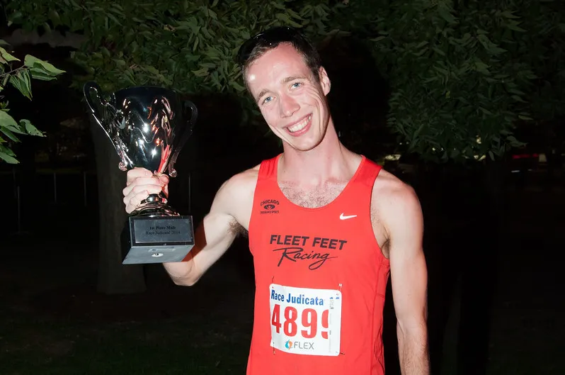 Jared after finishing a race for Fleet Feet, smiling holding a trophy.