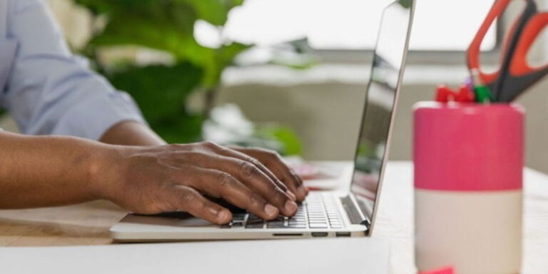 A close up of a man's hands over a keyboard on a desk typing.