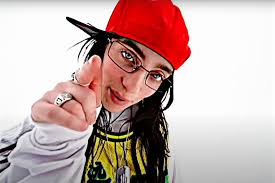 Singer Billie Eilish wearing a backwards cap pushed to the side, pointing her index finger right at the camera.